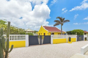 A yellow house with a red roof, surrounded by a white fence and a black gate. - NEW ! Casa Kudawecha (Casa and Casita) (Noord)