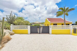 A gated property with a yellow building, a palm tree, and cacti. - NEW ! Casa Kudawecha (Casa and Casita) (Noord)