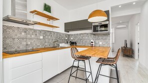 Una cucina moderna con isola in legno, due sgabelli da bar, una lampada a sospensione e uno schienale decorato.