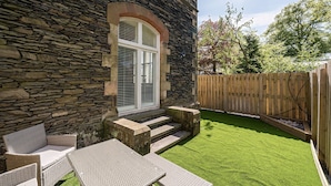 Un bâtiment en pierre doté d’une terrasse en bois, d’un espace extérieur aménagé pour s’asseoir et d’une pelouse bien entretenue.