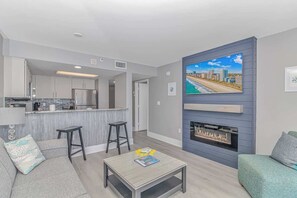 A modern living room with a fireplace, a kitchen in the background, and a cityscape view on the wall.