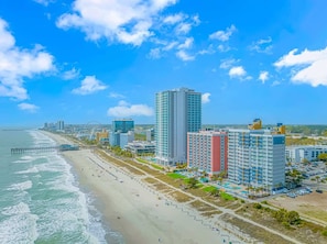 A coastal cityscape with a beach, high-rise hotels, and a pier.
