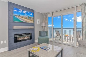 A modern living room with a TV, fireplace, and balcony with a view of the beach.