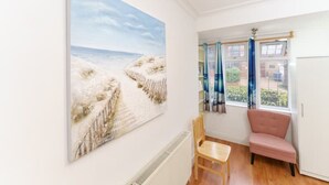 A room with a large beach painting, a chair, a pink sofa, and a window with curtains. - British Character in Golders Green. ground floor. 20min to oxford st. (London)
