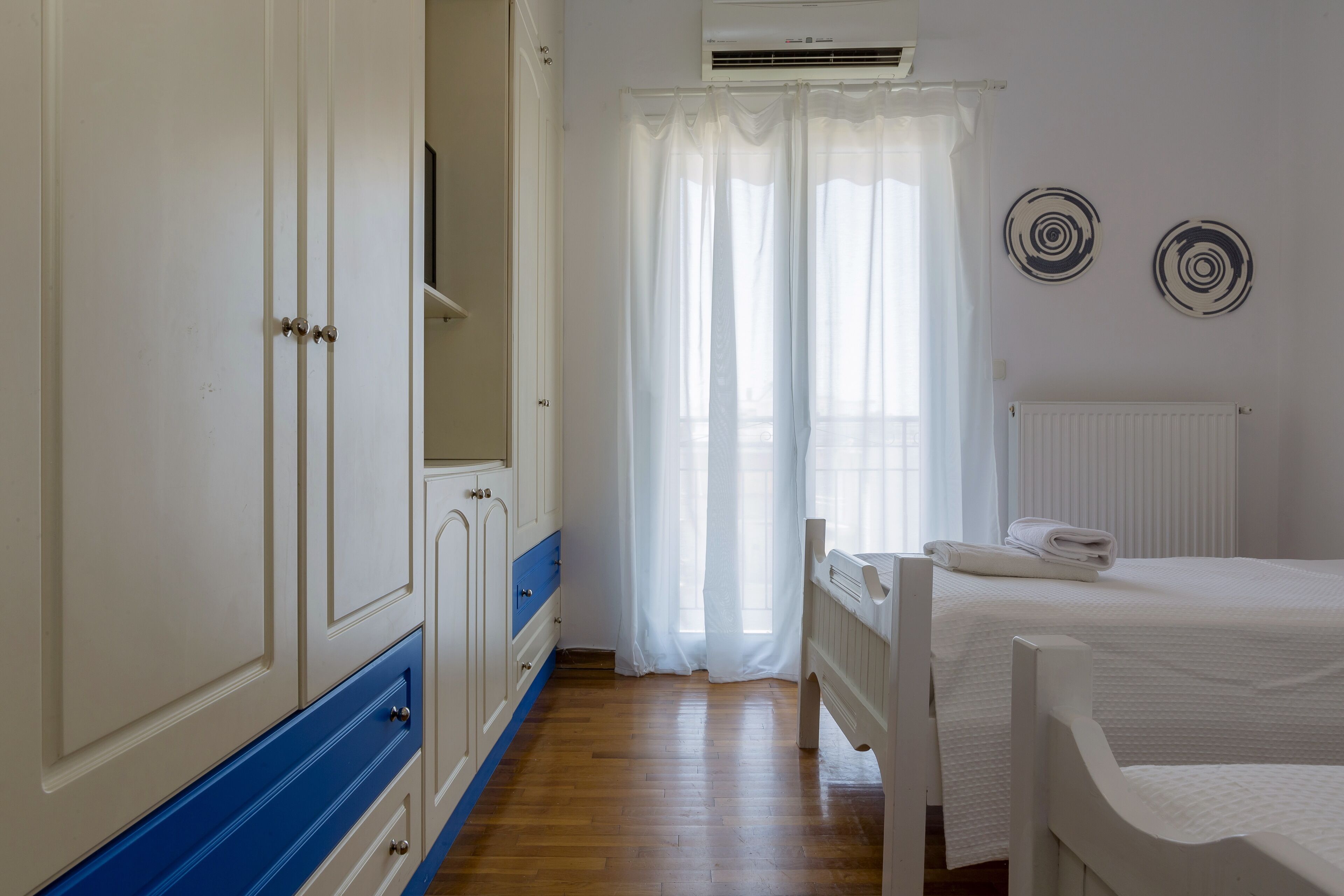 Un dormitorio con piso de madera, cama blanca y armario con detalles azules.