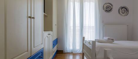 Un dormitorio con piso de madera, cama blanca y armario con detalles azules.