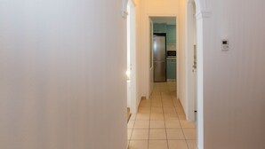 Un pasillo con paredes blancas y suelo de baldosas que conduce a una zona de cocina con un refrigerador y armarios.