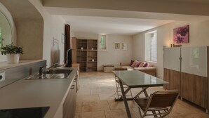 A modern kitchen with a dining area, wooden cabinets, a glass table, and a sofa with cushions.