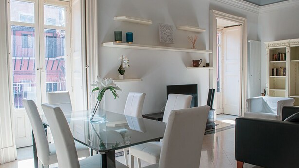 A modern living room with a glass dining table, white chairs, a black sofa, and a bookshelf. - Santa Domenica Guest house I (Catania)