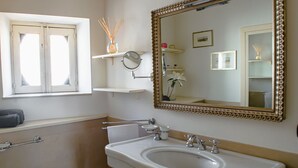 A bathroom with a pedestal sink, a large mirror with an ornate frame, and a window above the sink. - Santa Domenica Guest house I (Catania)