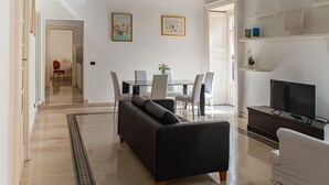 A modern living room with a black sofa, a glass dining table with chairs, a TV on a stand, and artwork on the walls. - Santa Domenica Guest house I (Catania)