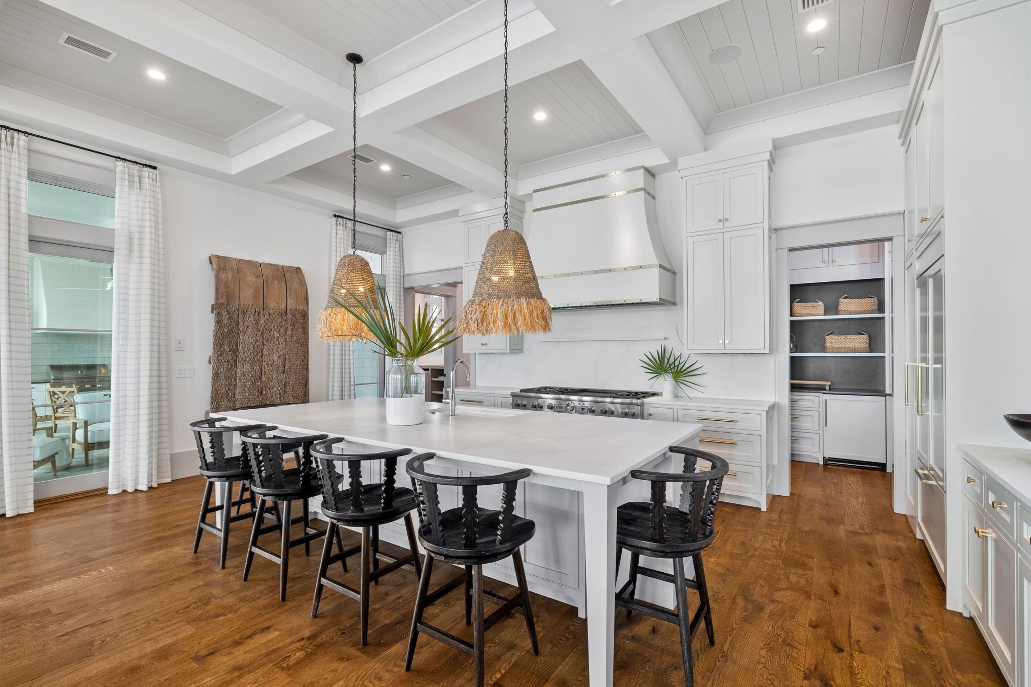 A modern kitchen with a large island, white cabinetry, and black bar stools.