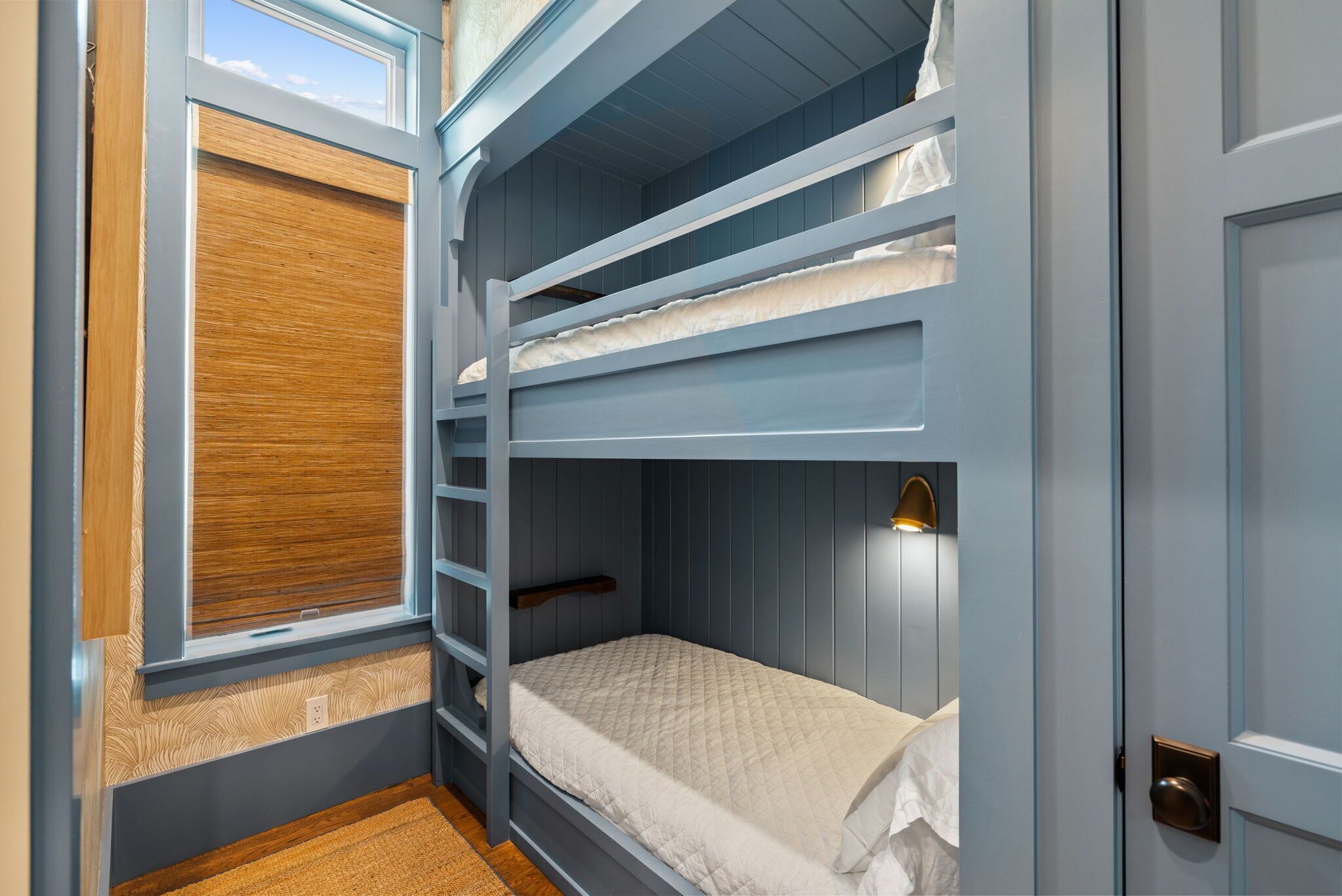 A bunk bed room with a window, a wooden blind, and a wall-mounted light fixture.