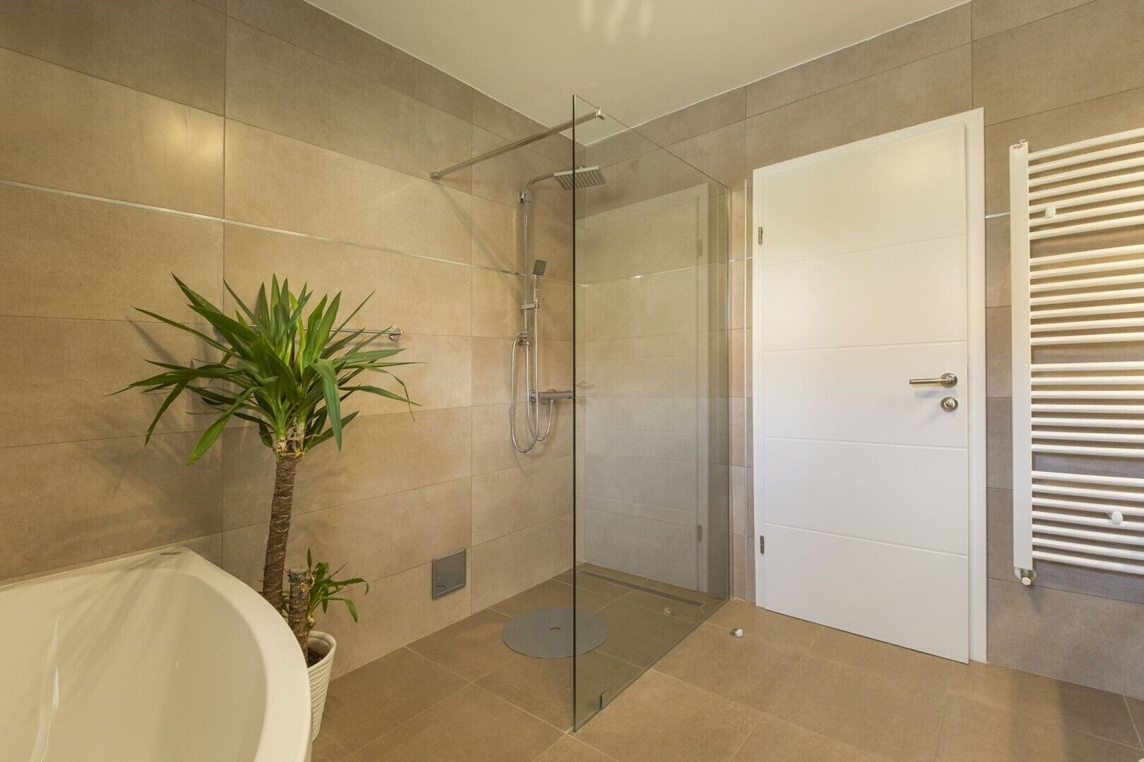 Un bagno moderno con doccia vetrata, una vasca da bagno bianca e una porta bianca.