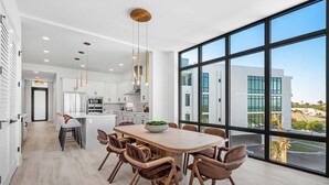 A modern kitchen with white cabinets, a wooden dining table, and a large window overlooking a building.