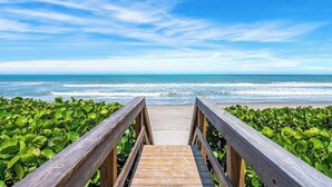 A wooden boardwalk leading to a beach with green foliage on either side.