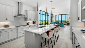 A modern kitchen with a large island, white cabinetry, and a view of the ocean.