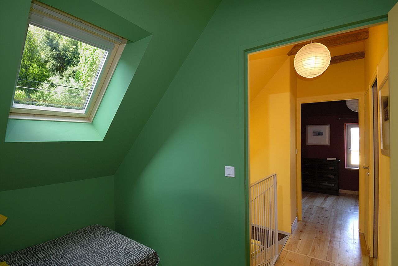 A room with a skylight, a bed, a hallway leading to another room, and a hanging light fixture.