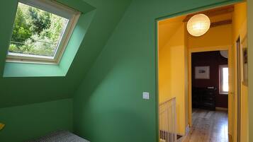 A room with a skylight, a bed, a hallway leading to another room, and a hanging light fixture.
