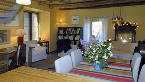 A cozy living room with a wooden dining table, white armchairs, a bookshelf, and a fireplace. - Gite de la Cascade, Pour 4 Personnes, Animaux Acceptés, Entre Rodez et Conques (Salles la source)