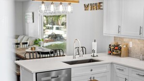 Una cocina moderna con armarios blancos, un lavavajillas de acero inoxidable y una mesa de comedor de madera.
