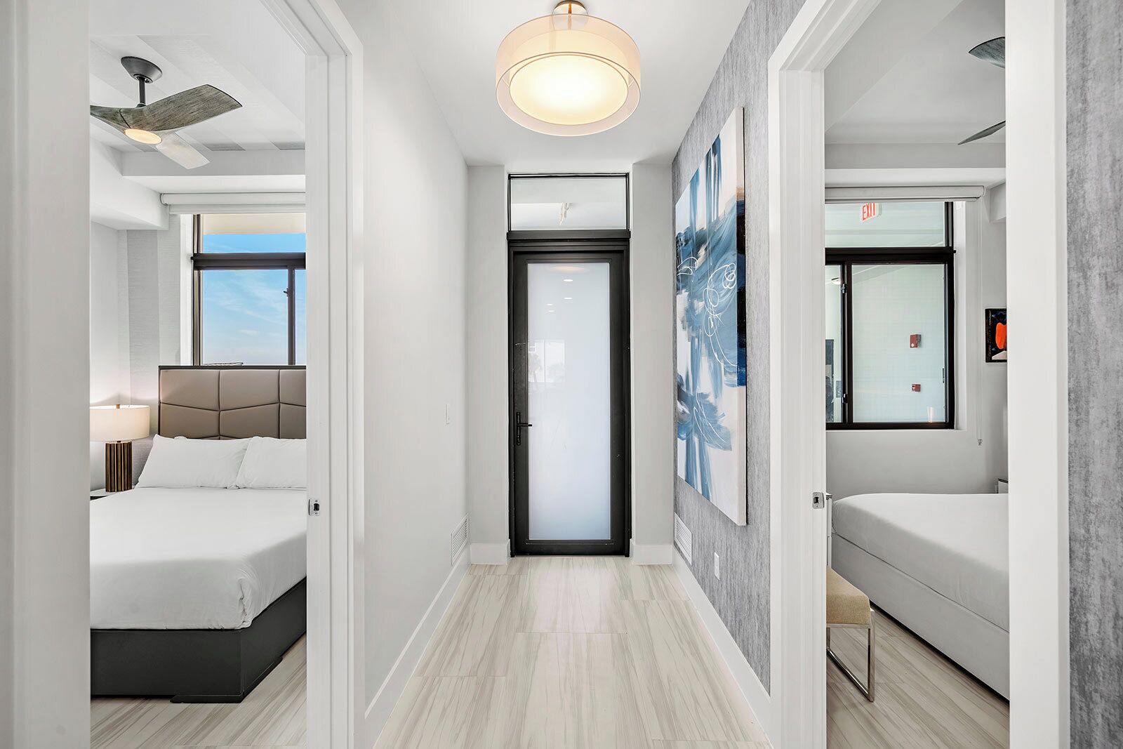 A modern hotel room with a bed, a desk, a ceiling fan, and a large window.