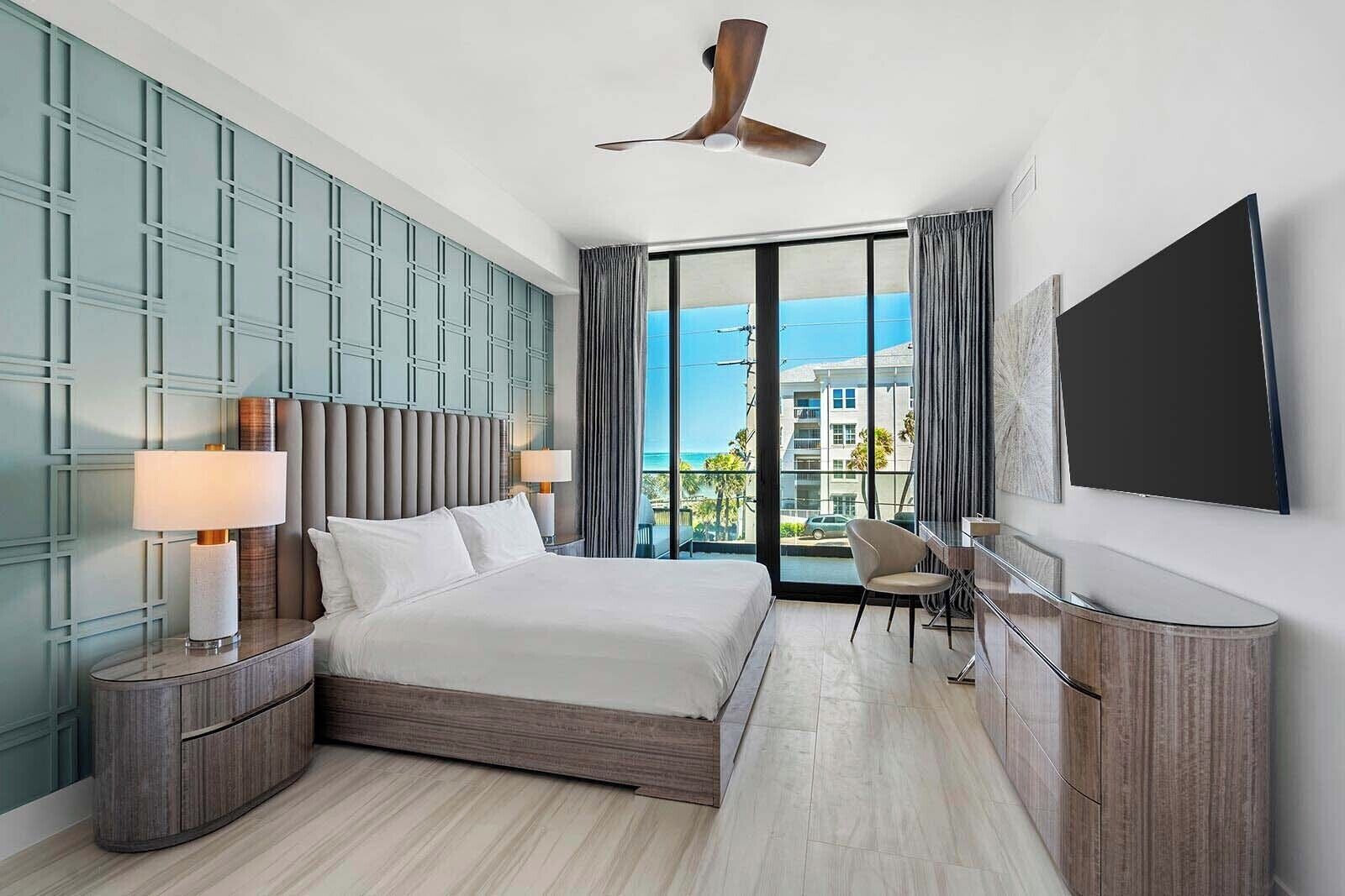 A modern hotel room with a large bed, a desk, a chair, and a TV.