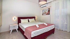 A neatly made bed with a red and white bedspread, a white nightstand with drawers, and a wall-mounted air conditioner. - Garitsa Gem Suite (Corfu)