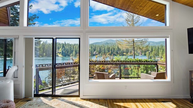 A spacious room with large windows offering views of a lake and forest. - Rivers Edge Retreat, Luxury Waterfront Estate, Private Dock, Fire pit, Swimming (Post Falls)