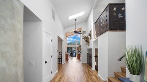 A spacious hallway with wooden flooring, a staircase, and a view of a mountain landscape through large windows. - Rivers Edge Retreat, Luxury Waterfront Estate, Private Dock, Fire pit, Swimming (Post Falls)