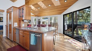 A modern kitchen with wooden cabinets, a central island with a sink, and a large sliding glass door leading to an outdoor area. - Rivers Edge Retreat, Luxury Waterfront Estate, Private Dock, Fire pit, Swimming (Post Falls)