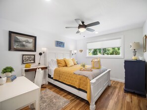 Quarto com cama, mesa de cabeceira, luminária, janela e ventilador de teto.