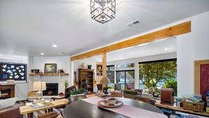 A spacious dining area with a large wooden table, surrounded by comfortable seating. A fireplace and bookshelves are visible in the background, with a view of the outdoors through large windows. - Rivers Edge Retreat, Luxury Waterfront Estate, Private Dock, Fire pit, Swimming (Post Falls)