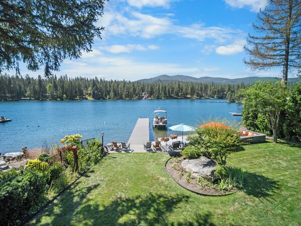 Um imóvel à beira do lago com um cais, área de estar externa e vista para o lago e a floresta ao redor.