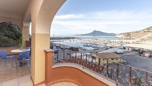Un balcón con vista a un puerto deportivo, barcos y una montaña distante.