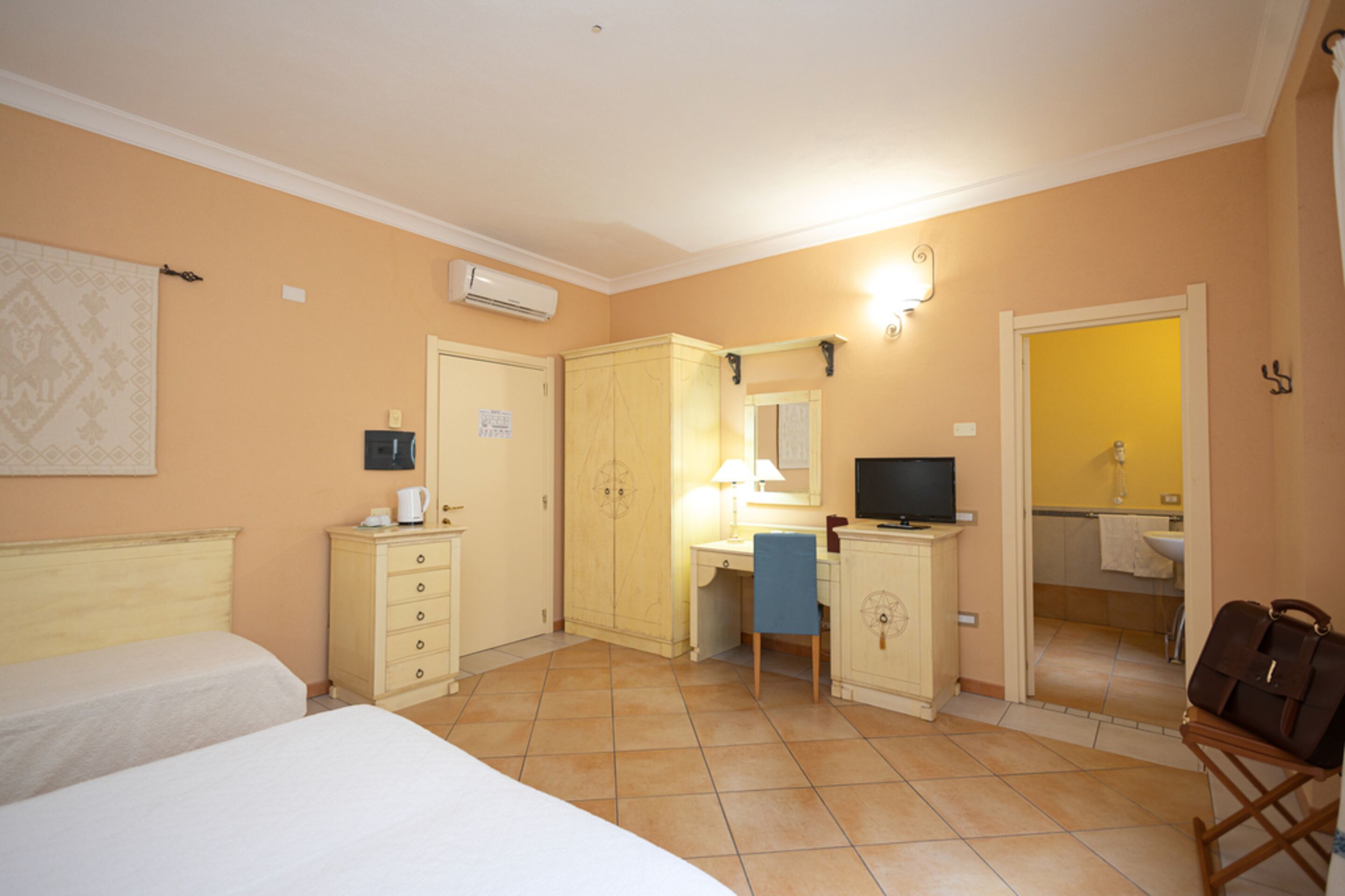 Een hotelkamer met twee bedden, een bureau met een stoel, een televisie en een badkamer die door een open deur zichtbaar is.