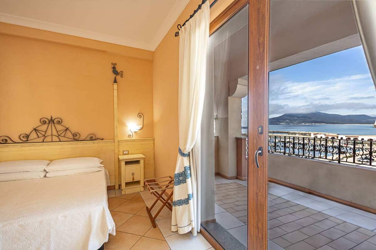 Ein Hotelzimmer mit Bett, Nachttisch, Lampe und einem Balkon mit Meerblick.