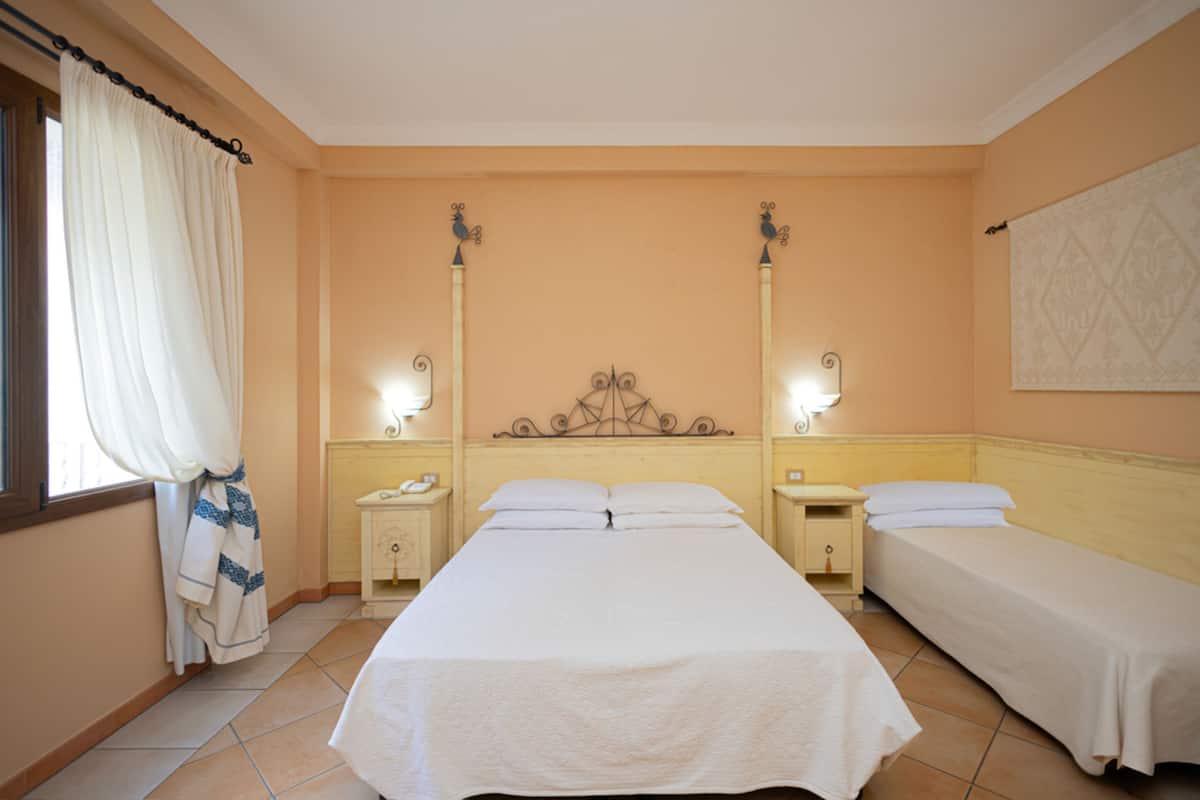 Ein Hotelzimmer mit einem großen Bett, zwei Nachttischen und einem Fenster mit Vorhängen.