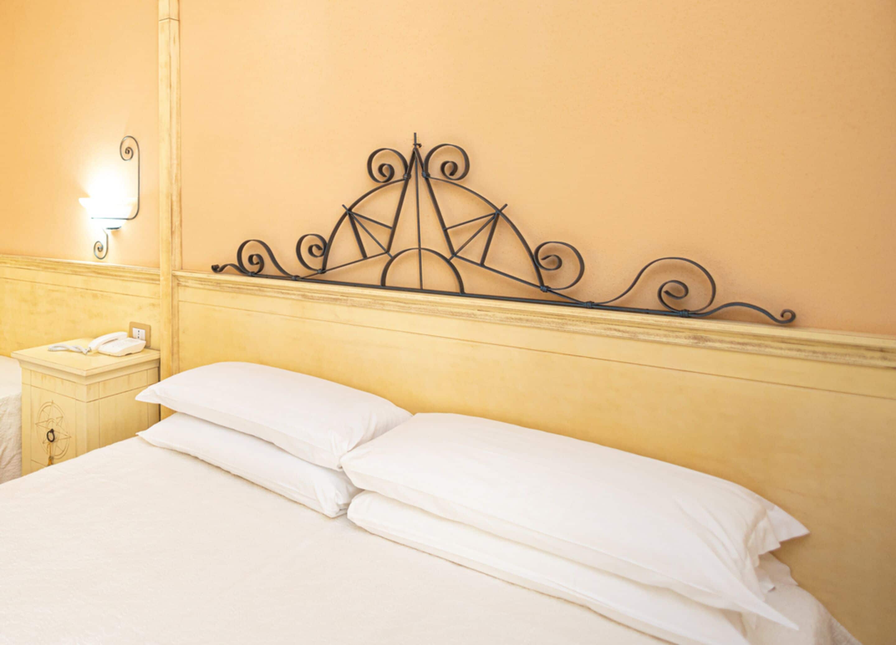 A bed with white linens and a metal headboard with a geometric design.