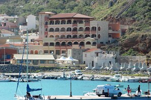 Una marina costera con barcos, una camioneta blanca y un edificio con varios balcones.