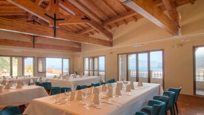 Un comedor con mesas dispuestas para una comida, ventanas amplias con vistas y vigas de madera en el techo.
