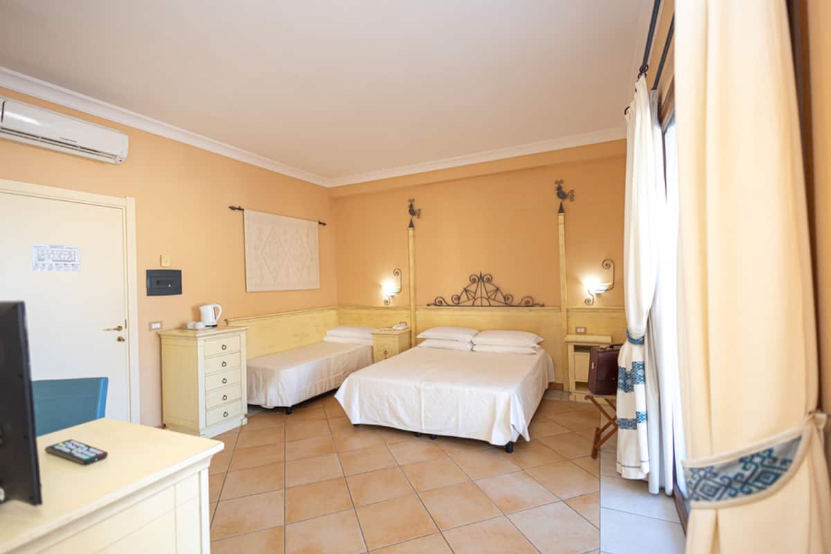 Ein Hotelzimmer mit zwei Betten, einem Schreibtisch mit Computer, einer Klimaanlage und einem Fenster mit Vorhängen.