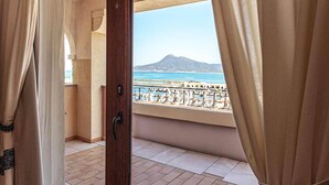 Una habitación con puerta de vidrio corrediza que da a un balcón con vistas al mar y a la montaña.