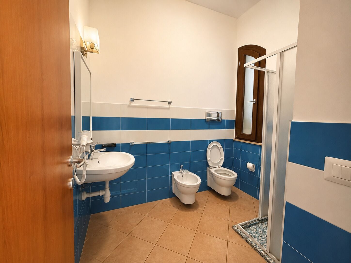 Een badkamer met een wastafel, twee toiletten, een toiletbrons en een douchegedeelte.