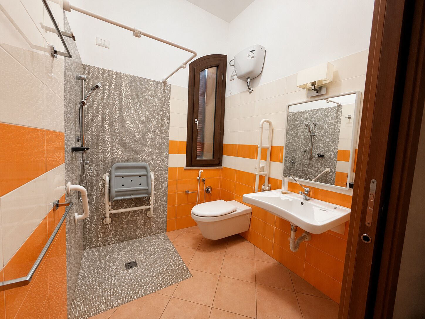 A bathroom with a shower, toilet, and sink, equipped with grab bars and a hand dryer.