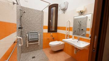 A bathroom with a shower, toilet, and sink, equipped with grab bars and a hand dryer.