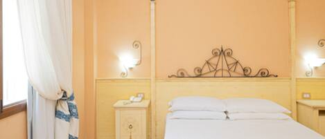 A bedroom with a bed, a nightstand, a lamp, and a window with curtains.