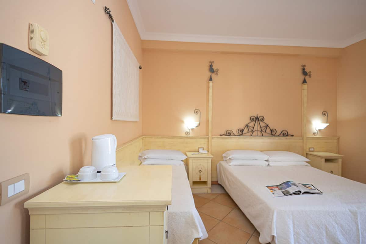 Ein Hotelzimmer mit zwei Betten, einem kleinen Schreibtisch, einer Kaffeemaschine, einer Lampe und einem an der Wand montierten Fernseher.