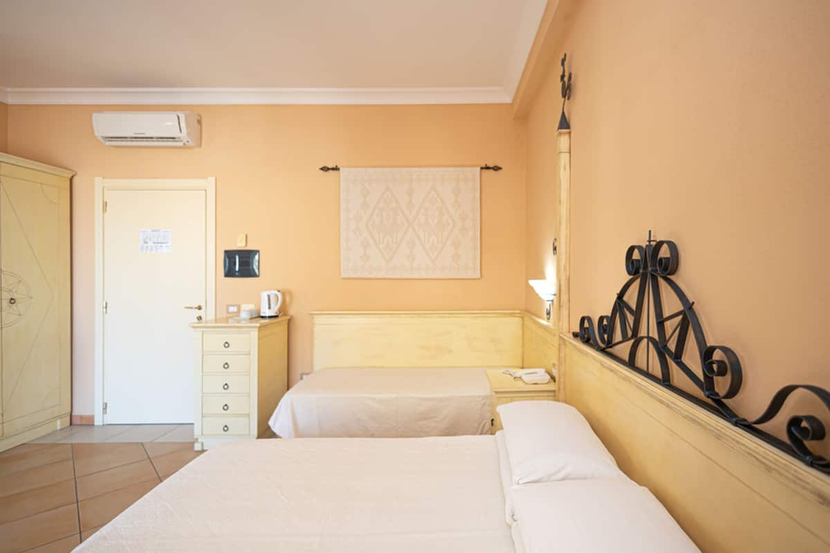 Ein Hotelzimmer mit zwei Betten, einem Schrank, einem Nachttisch mit Lampe und einer Wand-Klimaanlage.