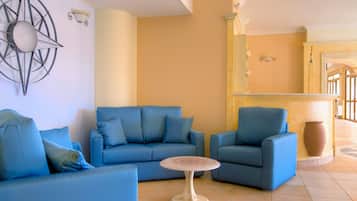 Un salon avec des canapés bleus et une table ronde, un élément décoratif mural et un plancher de couleur claire.